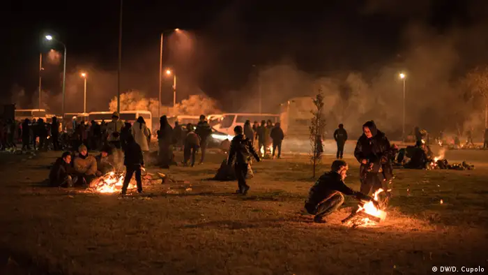 Migrants mull around and tend fires after nightfall at a Greek gas station