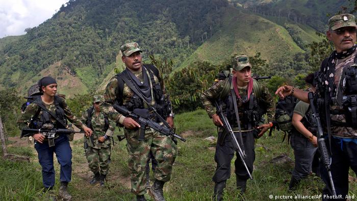 Men and women dressed in camouflage clothing carry machine guns in the rainforest 