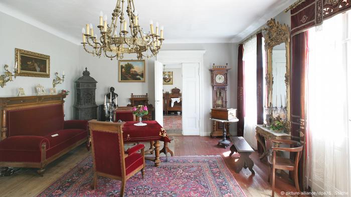 A view of a Gründerzeit parlour room with a sofa, chairs and carpets.