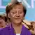 Chancellor Angela Merkel smiling as she holds a Bratwurst in a bread
