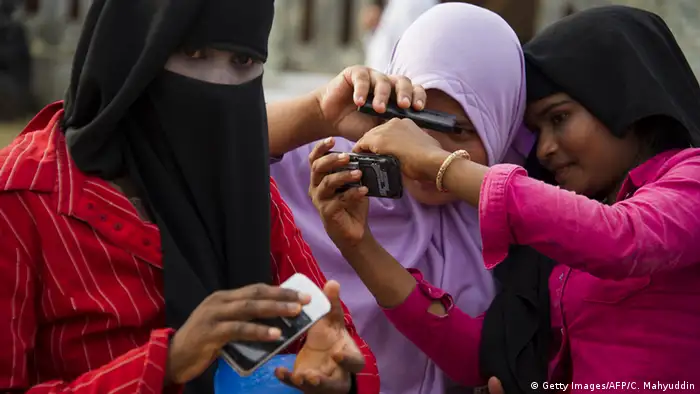 Three women wearing headscarves take photos with their phones