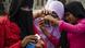 Three women wearing headscarves take photos with their phones