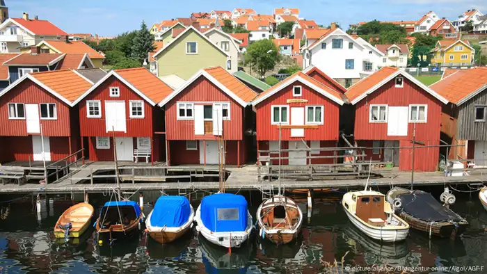 Sechs schwedische Reihenhäuser stehen an dem Ufer eines Sees. An dem Kai liegen einige kleienr Boote. (Foto: picture alliance/Bildagentur-online/Algol/AGF-F)