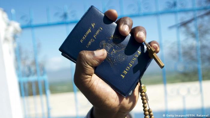 Foto simbólica de una mano de una persona afrodescendiente que sostiene un pasaporte estadounidense y un rosario.