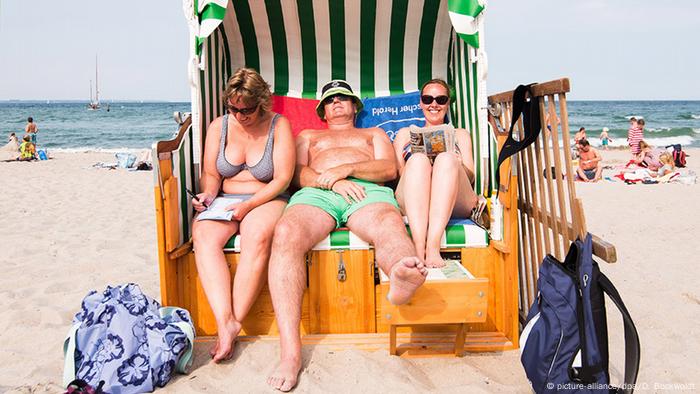Zwei Frauen und ein Mann sitzen am Strand in einem Strandkorb. (picture-alliance/dpa/D. Bockwoldt)
