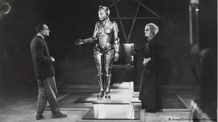Im Still aus dem Film Metropolis reicht Maschinenmensch Maria, neben ihrem Erfinder Rotwang stehend, ihre Hand Richtung Johann Fredersen aus. (Imago/EntertainmentPictures)