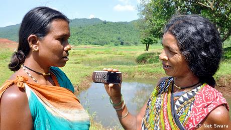 A woman speaks into a mobile phone held by another woman