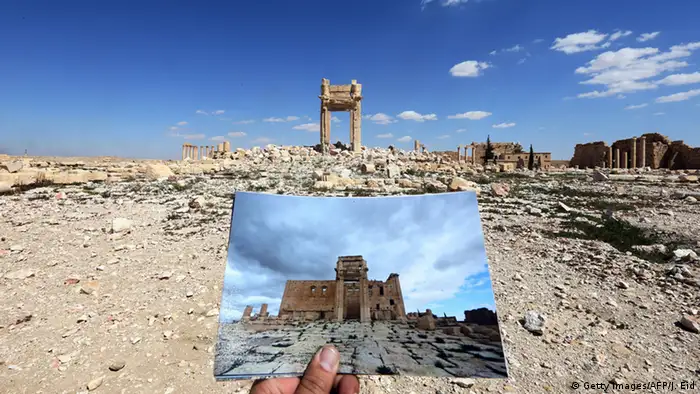 Ein Mensch hält eine Fotoaufnahme von vor der Zerstörung vor die aktuelle Sicht auf den Baal-Tempel (Foto: Getty Images)