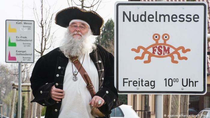 Rüdiger Weida von der Kirche der fliegenden Spaghettimonster neben seinem Schild «Nudelmesse» in Templin (Brandenburg) (Foto: picture-alliance/dpa/P. Pleul)
