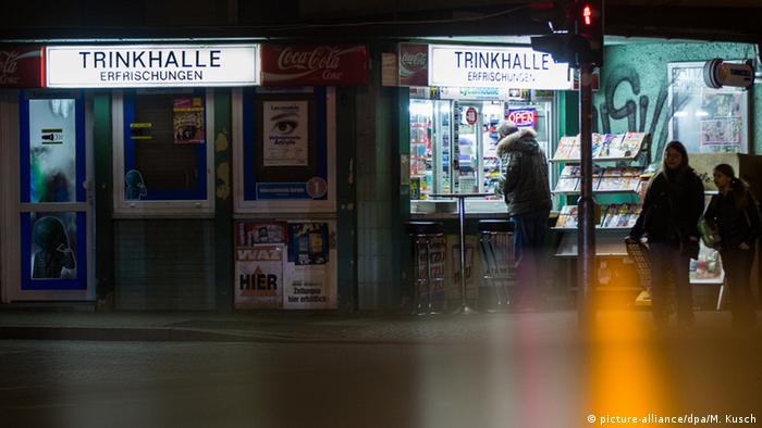 A person stands at the open window of a kiosk at night