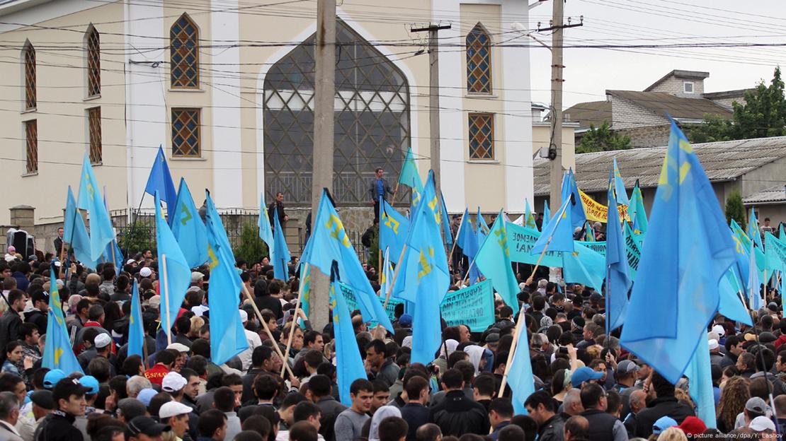 Multidão portando diversas bandeiras azuis diante de prédio que lembra um templo