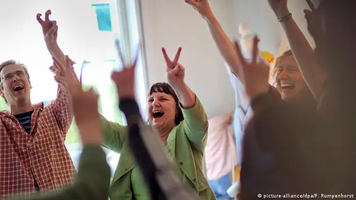 Männer und Frauen lachen in einer Gruppe gemeinsam und strecken Victory-Finger in die Luft. (Foto: picture-alliance/dpa/F. Rumpenhorst)