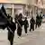 IS militants, dressed in black and carrying automatic rifles, march through Raqqa, Syria, their self-proclaimed capital.