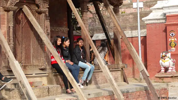 Mädchen sitzen unter abgestütztem Tempeldach am Durbar Square in Kathmandu