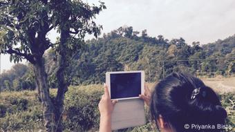 Foto: Eine junge Frau hält in einer bergigen, bewaldeten Gegend ein iPad in die Höhe.