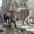 Syrien-Krieg: In Aleppo gehen Menschen vor einer völlig zerstörten Häuserwand an einem brennenden Auto vorbei (Foto: afp)