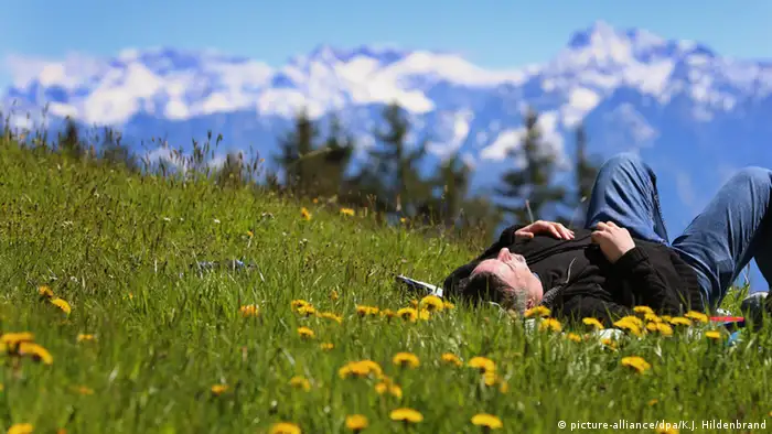 Hiker rests on a meadow in front of the panorama of the Alps