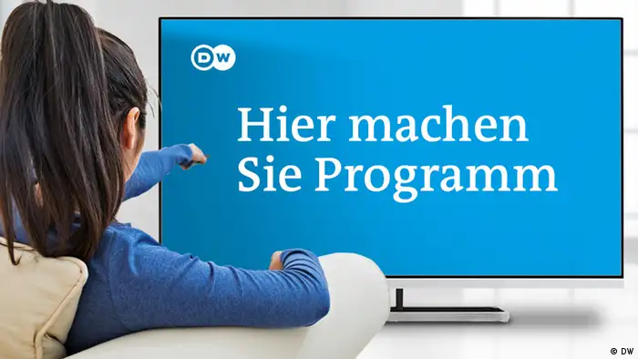 Eine junge Frau mit Pferdeschwanz sitzt auf einem Sessel vor einem Fernseher. Auf dem Bildschirm sind der Satz Hier machen Sie Programm und das DW Logo zu sehen.