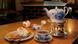 Teetasse, Kanne, Milchkännchen, Würfelzucker, eine Kerze und Waffeln mit Sahne auf einem Tisch Teetasse, Kanne, Milchkännchen, Würfelzucker, eine Kerze und Waffeln mit Sahne auf einem Tisch