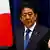 Japanese Prime Minister Shinzo Abe gestures during a speech, with a Japanese flag behind him.