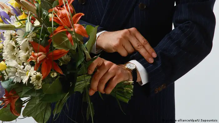 Man holding bouquet of flowers and looking at his watch