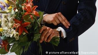 Mann hält Blumenstrauß und guckt auf die Armbanduhr
