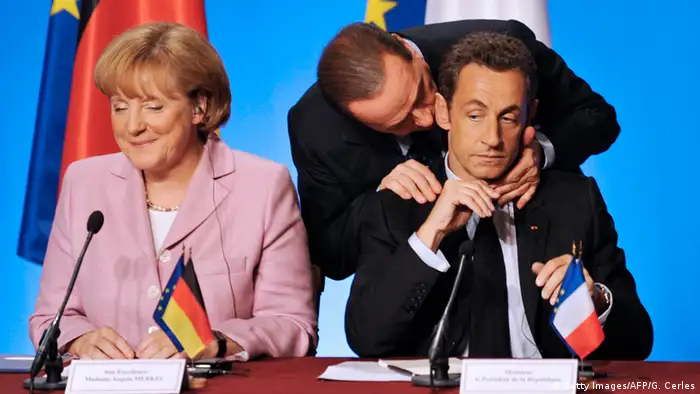 Silvio Berlusconi umarmt Nicolas Sarkozy neben Angela Merkel