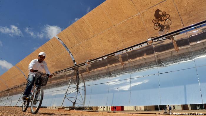 A Moroccan engineer cycles past the solar panels of a solar power station