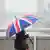 Großbritannien London Frau geht mit Union Jack Regenschirm über die Tower Bridge