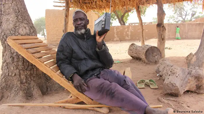 Seydou Ilboudo sits in a wooden chair and listens to the radio