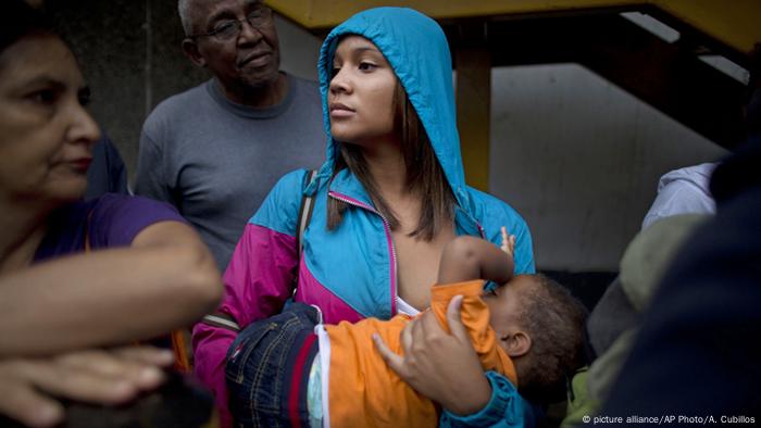 Una madre amamanta a su hijo mientras espera en la fila de un supermercado en Caracas. (Archivo).