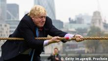 Boris Johnson zieht vor der der Kulisse der Londoner Innenstadt angestrengt an einem Tau