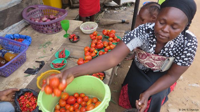 A women holds up a bucket of tomatoes at a market