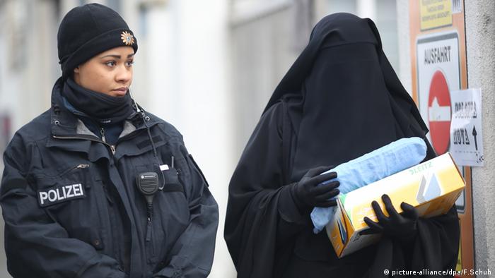 Женщина с полностью закрытыми покрывалом лицом и телом рядом с полицейским 