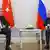 Sitting, Turkish President Recep Tayyip Erdogan talks with Russian President Vladimir Putin, with their respective flags behind them.