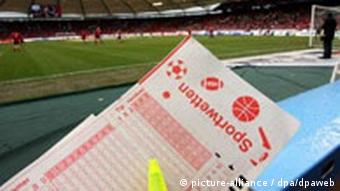 A betting form held up in front of a socer pitch