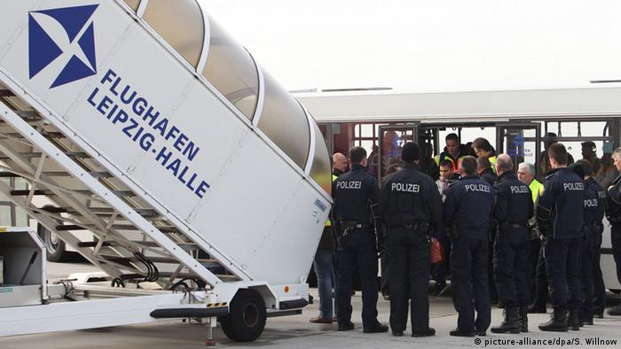 Police officers in front of a bus carrying rejected migrants to an airplane