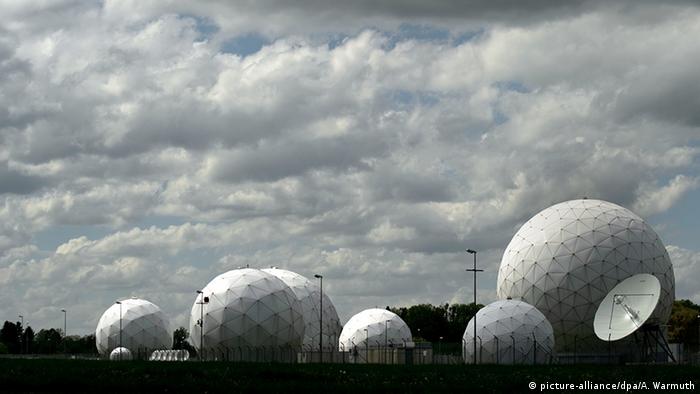 Riesige weiße Radarkuppeln, die aussehen wie gigantische Bälle, befinden sich hinter Stacheldrahtzaun.