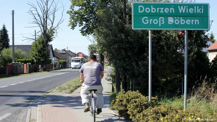 A man rides a bike passed a signpost for the town of Dobrzeń Wielki 