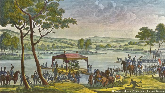 александровка в германии история. 19557432 303. александровка в германии история фото. александровка в германии история-19557432 303. картинка александровка в германии история. картинка 19557432 303. В северной части Потсдама есть место столь русское, какой даже сама Россия никогда не была. Тринадцать типично русских изб, щедро украшенных резьбой, стоят здесь одна возле другой и позади каждой — большой фруктовый сад. Некоторые дома красуются в несколько этажей, а те, что поскромнее, рассредоточены по краям. Кто-то торгует здесь огурцами, кто-то — яблоками. В затесавшемся меж построек кафе подают солянку. Построены эти дома были в 1826 году. Аутентичными они не были никогда.Поселок называется Александровкой, поскольку построен по приказу прусского короля Фридриха Вильгельма III в память о царе Александре I, которым его связывали переменчивые отношения — они были и друзьями, и врагами. В 1812 году король Пруссии взял в плен 62 русских солдата и доставил в Потсдам. Говорят, его тронули их меланхоличные напевы,они стали его солдатским хором и сопровождали прусское войско, развлекая его «песнями с тамбурином и маленькими колокольчиками». Когда Россия и Пруссия стали друзьями, солдаты так и остались при королевском дворе в Потсдаме — царь преподнес их Фридриху Вильгельму в качестве подарка. Ради оставшейся дюжины человек и построили Александровку. Ансамбль срубов, украшенных резными орнаментами, флюгерами, зубчатыми фризами. Этот фронтон принадлежит самому великолепному дому в центре поселка — в нем жил смотритель колонии.Король лично разработал вместе с Петером Йозефом фон Ленне план поселка, имеющий форму ипподрома, рассеченного Андреевским крестом; часть домов стоят напротив друг друга, другие на большом расстоянии.Каждый из певцов русского солдатского хора получил собственный дом со всем хозяйством — вплоть до глиняных горшков, огромным садом, огородом и коровой. От уплаты налогов они были освобождены. Идея была возвышенной, вот только не слишком функциональной. Солдаты не были крестьянами, они не могли себя обеспечивать, прилично выпивали и все чаще слали просительные письма. Вскоре им было разрешено зарабатывать деньги иначе: они стали сдавать комнаты тем берлинцам, что летом стремились попасть в иной, фольклорный мир.За каждым домом простирается большой участок, с которого солдатские певцы должны были кормиться.Курьез не только в том, что в социальном плане поселок не действовал. По сути, в нем есть что-то от Диснейленда; это не русская, а потемкинская деревня: сами срубы таковыми не являются, а представляют собой фахверковые дома, обитые деревом. Деревянная резьба не является традиционно крестьянской, а берет свое начало, скорее, в романтических идеях XIX века. Ее прообразом послужила другая образцовая деревня под Санкт-Петербургом — Глазово. Даже членение чудесного фасада не аутентично и не практично: там, где обозначен главный вход, войти в дом, как правило, невозможно — можно только сбоку. Так что не всегда можно выйти прямо на веранду. Не случайно позднее баварский Король Людвиг II построил Нойшванштайн, идеализированный рыцарский замок: романтика, идеализация сельской жизни и средневековья оставили отпечаток на времени и его искусствах. Так что Александровка соотносится не столько с Россией, сколько с эпохой, в которую возникла.Так выглядела деревня между 1928 и 1944 годами, запечатленная Максом Бауэром.В то время, как одни дома имеют два этажа, другие (особенно те, что по краям поселка) выглядят скромнее. Принцип, однако, один и тот же: имитация сруба и традиционного декора плюс фантазия.На холме возвышается выкрашенный в умилительный розовый цвет православный храм Александра Невского, построенный вместе с поселком и для него предназначенный. Внутри мерцают русские иконы, пахнет ладаном и звучит запись мужского хора.Некогда Александровка была популярным туристическим объектом, но со временем дела пошли все хуже. Хотя архитектурный ансамбль еще во времена ГДР был взят под охрану памятников, сохранился он плохо. Отдельные дома постепенно пришли в упадок, территория заросла, была застроена садовыми домиками. Позже через деревню чуть было не проложили трамвайную линию — сейчас она ее огибает.После объединения Германии инициативы по охране памятников докатились и до деревни. В одном из домов был открыт музей, снова были вытащены на свет божий старинные планы Ленне. Вместо 574 старых фруктовых деревьев были посажены новые. В роскошном доме смотрителя сегодня обосновалось кафе. Большинство домов стали частными — в трех из них до 2013 года еще жили потомки тех самых певцов солдатского хора (с давних пор эти дома не разрешается продавать, а только передавать по наследству, причем по прямой мужской линии). В одном из домов был создан чудесный маленький музей. Так что сегодня Александровка снова превратилась в нарядную идиллию. В жаркие летние дни случается непомерно широкому туристическому автобусу проехать по длинным и обычно пустынным улицам, пересекающимся в виде Андреевского креста. В остальном кажется, что время здесь остановилось. Но это, в сущности, время, которого никогда не было. александровка в германии история. 19557432 303. александровка в германии история фото. александровка в германии история-19557432 303. картинка александровка в германии история. картинка 19557432 303. В северной части Потсдама есть место столь русское, какой даже сама Россия никогда не была. Тринадцать типично русских изб, щедро украшенных резьбой, стоят здесь одна возле другой и позади каждой — большой фруктовый сад. Некоторые дома красуются в несколько этажей, а те, что поскромнее, рассредоточены по краям. Кто-то торгует здесь огурцами, кто-то — яблоками. В затесавшемся меж построек кафе подают солянку. Построены эти дома были в 1826 году. Аутентичными они не были никогда.Поселок называется Александровкой, поскольку построен по приказу прусского короля Фридриха Вильгельма III в память о царе Александре I, которым его связывали переменчивые отношения — они были и друзьями, и врагами. В 1812 году король Пруссии взял в плен 62 русских солдата и доставил в Потсдам. Говорят, его тронули их меланхоличные напевы,они стали его солдатским хором и сопровождали прусское войско, развлекая его «песнями с тамбурином и маленькими колокольчиками». Когда Россия и Пруссия стали друзьями, солдаты так и остались при королевском дворе в Потсдаме — царь преподнес их Фридриху Вильгельму в качестве подарка. Ради оставшейся дюжины человек и построили Александровку. Ансамбль срубов, украшенных резными орнаментами, флюгерами, зубчатыми фризами. Этот фронтон принадлежит самому великолепному дому в центре поселка — в нем жил смотритель колонии.Король лично разработал вместе с Петером Йозефом фон Ленне план поселка, имеющий форму ипподрома, рассеченного Андреевским крестом; часть домов стоят напротив друг друга, другие на большом расстоянии.Каждый из певцов русского солдатского хора получил собственный дом со всем хозяйством — вплоть до глиняных горшков, огромным садом, огородом и коровой. От уплаты налогов они были освобождены. Идея была возвышенной, вот только не слишком функциональной. Солдаты не были крестьянами, они не могли себя обеспечивать, прилично выпивали и все чаще слали просительные письма. Вскоре им было разрешено зарабатывать деньги иначе: они стали сдавать комнаты тем берлинцам, что летом стремились попасть в иной, фольклорный мир.За каждым домом простирается большой участок, с которого солдатские певцы должны были кормиться.Курьез не только в том, что в социальном плане поселок не действовал. По сути, в нем есть что-то от Диснейленда; это не русская, а потемкинская деревня: сами срубы таковыми не являются, а представляют собой фахверковые дома, обитые деревом. Деревянная резьба не является традиционно крестьянской, а берет свое начало, скорее, в романтических идеях XIX века. Ее прообразом послужила другая образцовая деревня под Санкт-Петербургом — Глазово. Даже членение чудесного фасада не аутентично и не практично: там, где обозначен главный вход, войти в дом, как правило, невозможно — можно только сбоку. Так что не всегда можно выйти прямо на веранду. Не случайно позднее баварский Король Людвиг II построил Нойшванштайн, идеализированный рыцарский замок: романтика, идеализация сельской жизни и средневековья оставили отпечаток на времени и его искусствах. Так что Александровка соотносится не столько с Россией, сколько с эпохой, в которую возникла.Так выглядела деревня между 1928 и 1944 годами, запечатленная Максом Бауэром.В то время, как одни дома имеют два этажа, другие (особенно те, что по краям поселка) выглядят скромнее. Принцип, однако, один и тот же: имитация сруба и традиционного декора плюс фантазия.На холме возвышается выкрашенный в умилительный розовый цвет православный храм Александра Невского, построенный вместе с поселком и для него предназначенный. Внутри мерцают русские иконы, пахнет ладаном и звучит запись мужского хора.Некогда Александровка была популярным туристическим объектом, но со временем дела пошли все хуже. Хотя архитектурный ансамбль еще во времена ГДР был взят под охрану памятников, сохранился он плохо. Отдельные дома постепенно пришли в упадок, территория заросла, была застроена садовыми домиками. Позже через деревню чуть было не проложили трамвайную линию — сейчас она ее огибает.После объединения Германии инициативы по охране памятников докатились и до деревни. В одном из домов был открыт музей, снова были вытащены на свет божий старинные планы Ленне. Вместо 574 старых фруктовых деревьев были посажены новые. В роскошном доме смотрителя сегодня обосновалось кафе. Большинство домов стали частными — в трех из них до 2013 года еще жили потомки тех самых певцов солдатского хора (с давних пор эти дома не разрешается продавать, а только передавать по наследству, причем по прямой мужской линии). В одном из домов был создан чудесный маленький музей. Так что сегодня Александровка снова превратилась в нарядную идиллию. В жаркие летние дни случается непомерно широкому туристическому автобусу проехать по длинным и обычно пустынным улицам, пересекающимся в виде Андреевского креста. В остальном кажется, что время здесь остановилось. Но это, в сущности, время, которого никогда не было.