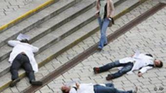 Männer in weißen Kitteln liegen auf dem Boden, während eine Passantin vorbeigeht (Foto: AP)