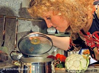 Eine Frau hebt in der Küche am Herd den Deckel eines Kochtopfes und schaut in den Topf (Foto: DPA)