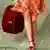 A women walks in an orange skirt walks with a suitcase in her hand