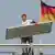 Prognoza e tregtisë së jashtme gjermane flet për rritje eksportesh. Ne foto: nje punetor mban nje pllake metalike ne dore dhe kalon para Rajshtagut ne Berlin (flamuri ne sfond)