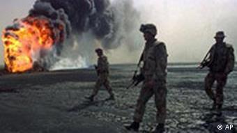 A US Marine patrol walks across the charred oil landscape near a burning well during perimeter security patrol near Kuwait City