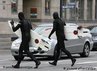 Two surfers in wetsuits cross a busy street with their surfboards