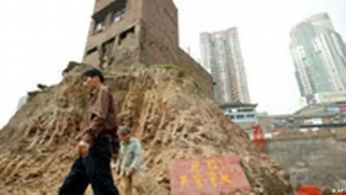 ** FILE ** People walk past a house sitting on a mound in the middle of a construction site in Chongqing, in southwest China, Thursday, March 22, 2007. The family who occupy the house refused an offer of compensation from the land developer, but was ordered by the local court to move out. The Chinese couple who own it have stirred up an Internet and media frenzy over their fight to keep their home and restaurant from being razed by developers, in what is seen as the first major test of a newly passed private property law. (AP Photo/EyePress, File) ** CHINA OUT **