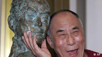 The Dalai Lama smiles next to a bust of himself