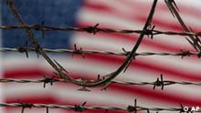 A flag waves behind the barbed and razor-wire at the detention compound on Guantanamo Bay U.S. Naval Base in Cuba, Wednesday, Oct. 10, 2007. The U.S. military is reviewing its decision to classify hundreds of Guantanamo Bay inmates as enemy combatants, a step that could lead to new hearings for men who have spent years behind bars in indefinite detention. (AP Photo/Brennan Linsley)