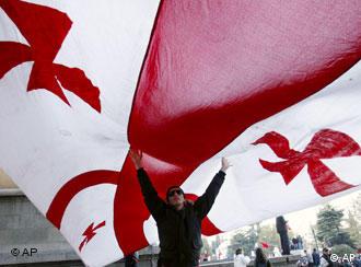 A figure stands under a giant Georgian flag